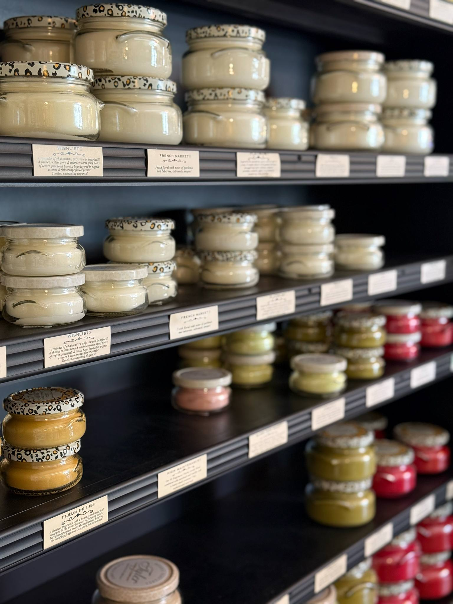Wall display of Tyler Candle Company products at Shoppes on Davis, featuring signature glass jar candles, scent sachets, and glamorous fragrance gifts.