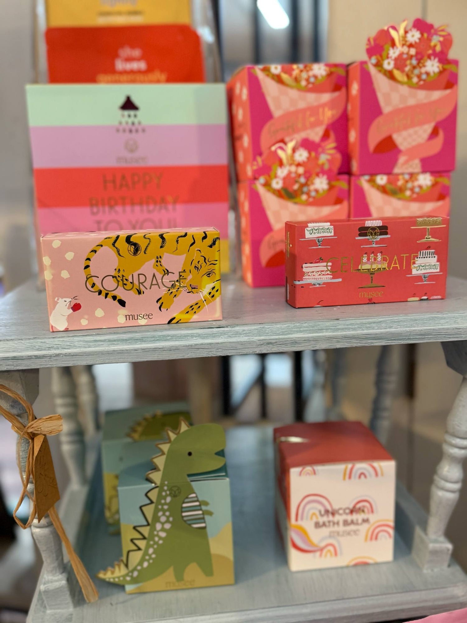 Colorful Musee bath balms and soaps on display at Shoppes on Davis, featuring playful packaging with themes like Courage, Celebrate, Dinosaur, Unicorn, and Happy Birthday.